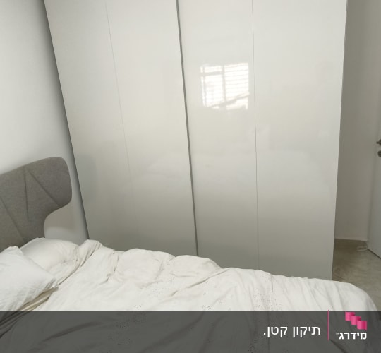 ארון בגדים לבן ליד מיטה עם מצעים לבנים